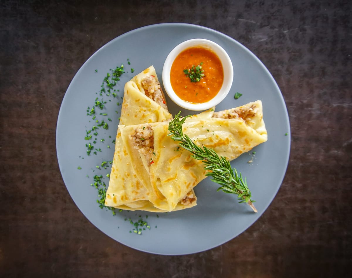 Folded savoury crepes plated with house red sauce
