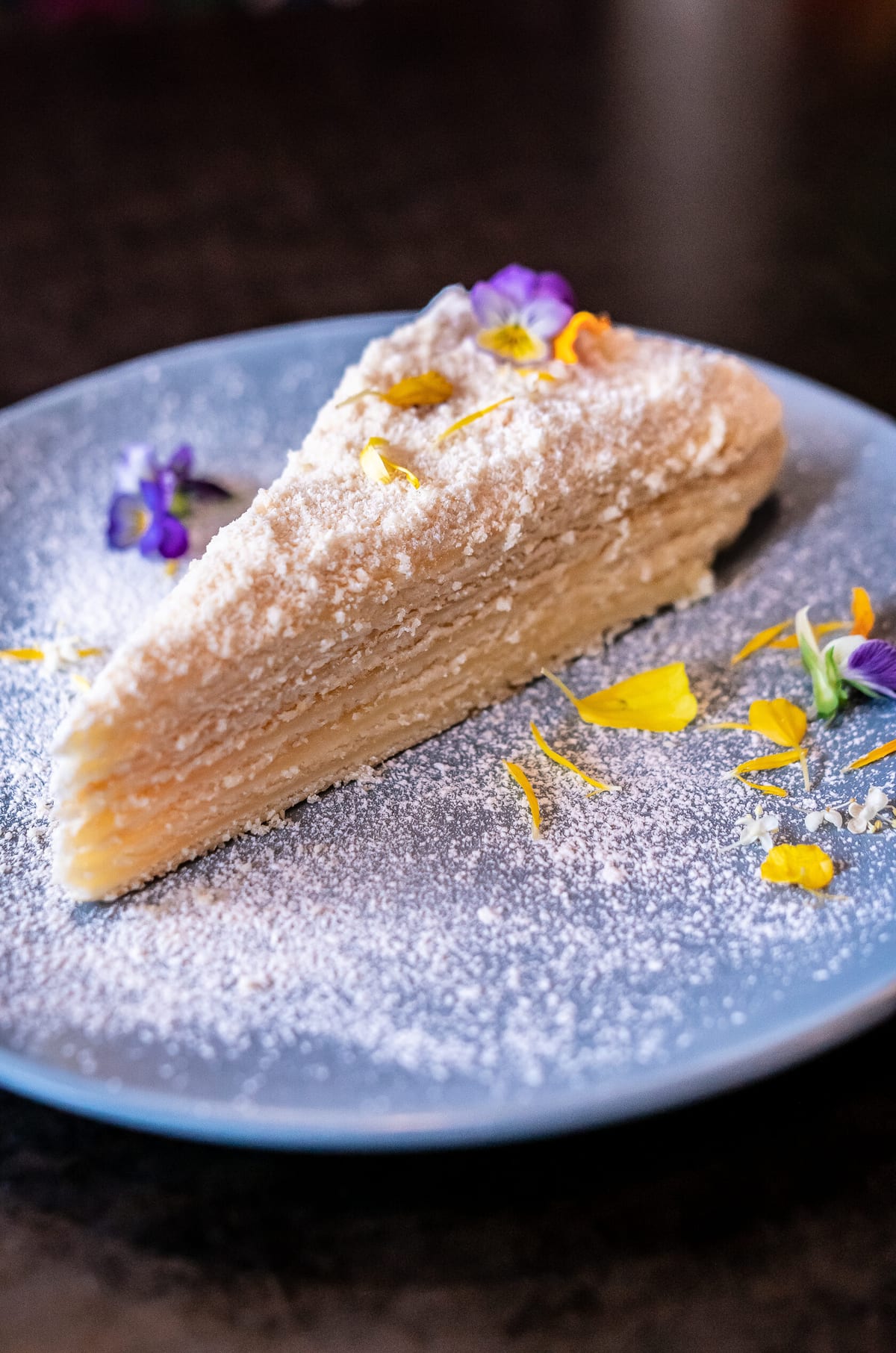 A slice of Medovik honey cake, dusted and finished with edible flowers