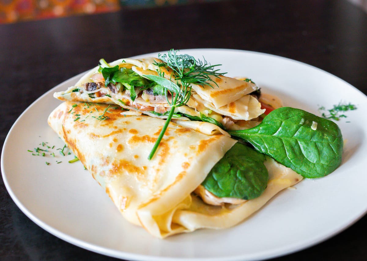 A savoury crepe folded with mushroom, cheese and greens on a white plate