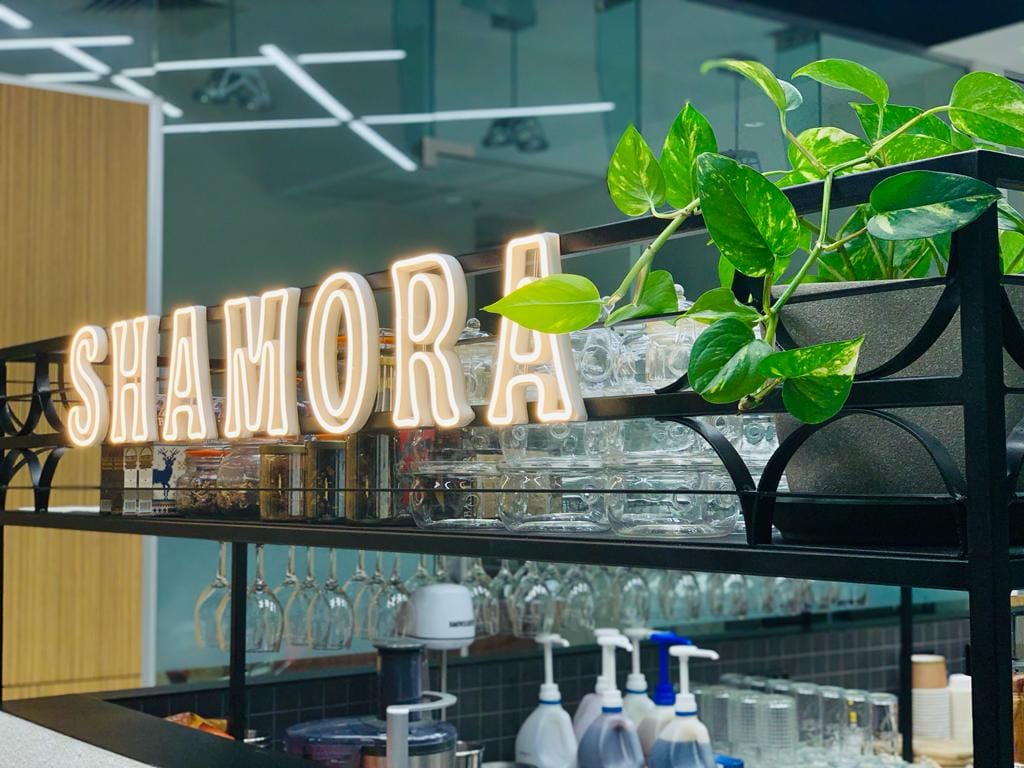 The illuminated Shamora sign behind the cafe bar, with a trailing pothos plant